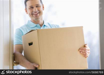 Happy man carrying cardboard box at entrance of new house