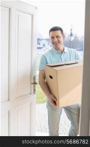 Happy man carrying cardboard box while entering new house