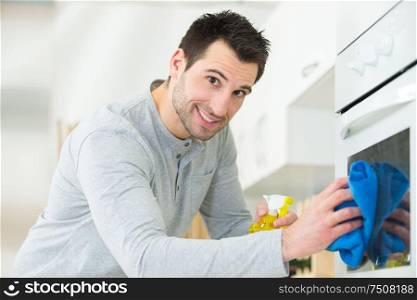 happy man cleaning domestic oven in kitchen