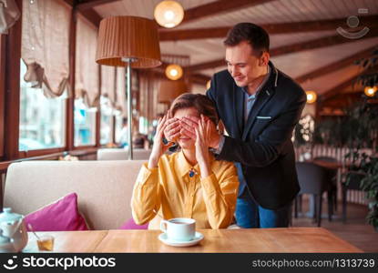 Happy man closes eyes hands to beautiful woman in restaurant. Romantic date of love couple