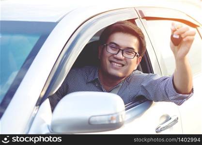 Happy man driver showing car keys and leaning on car door