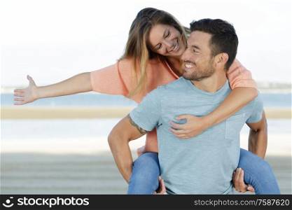 happy man giving woman piggyback on beach