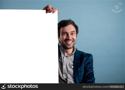 Happy man holding a white poster.Happy smiling young man showing blank signboard with empty copyspace area for slogan or advertising text message. Caucasian male model in advertisiment concept.. Happy smiling man showing blank signboard with empty copyspace area for slogan or advertising text message.
