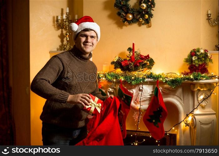 Happy man holding red Santa bag with presents at fireplace