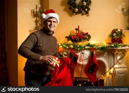 Happy man holding red Santa bag with presents at fireplace