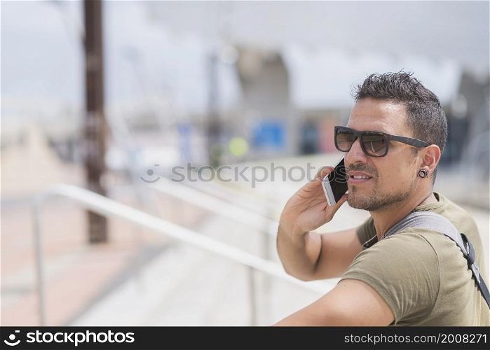 Happy man in sunglasses standing outdoors, talking by smartphone
