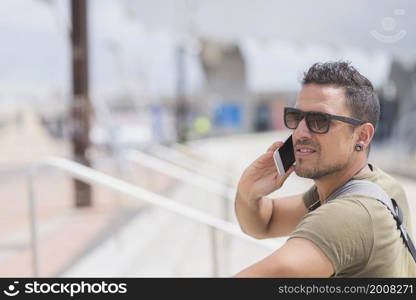 Happy man in sunglasses standing outdoors, talking by smartphone