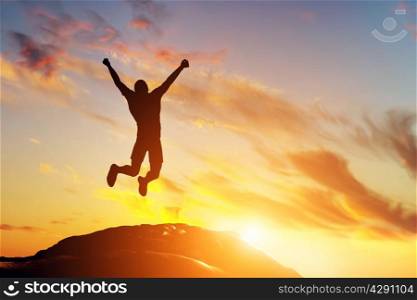 Happy man jumping for joy on the peak of the mountain, cliff at sunset. Success, winner, happiness