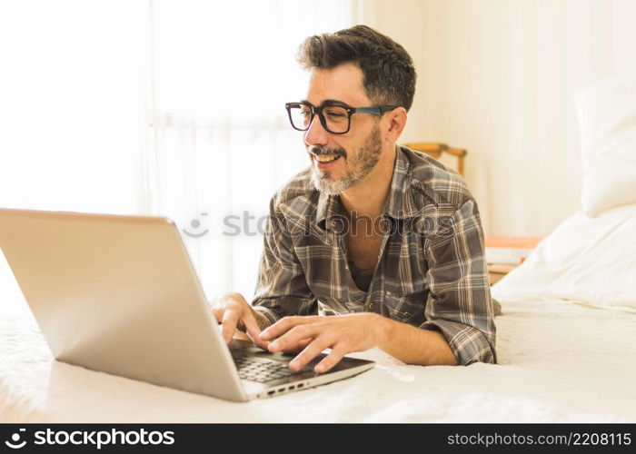 happy man lying cozy bed using laptop