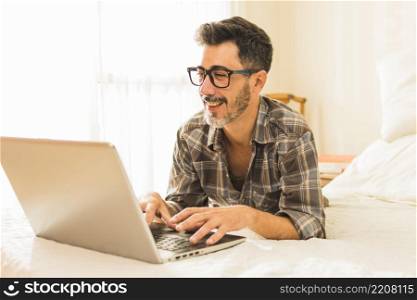 happy man lying cozy bed using laptop