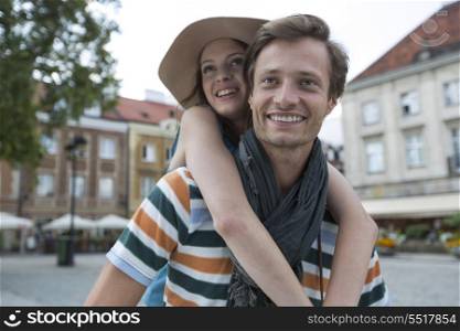Happy man piggybacking woman on street during vacation