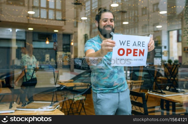 Happy man placing opening poster after coronavirus on the glass of his business. Man placing opening poster after coronavirus