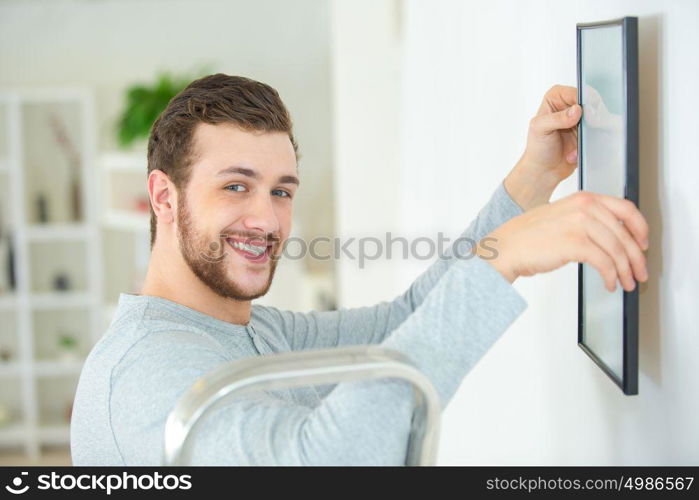 happy man positioning picture frame on wall