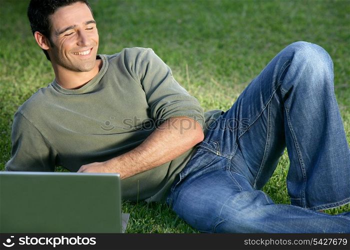 Happy man sat in field with laptop