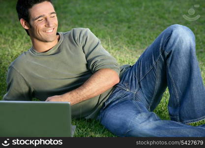 Happy man sat in field with laptop