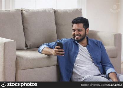 Happy man sitting at home and looking at his phone. 