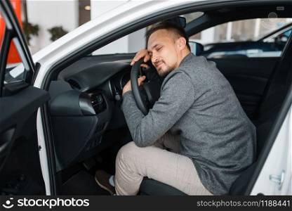 Happy man sitting in new car, showroom. Male customer choosing vehicle in dealership, automobile sale, auto purchase. Happy man sitting in new car, showroom