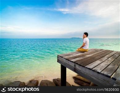 happy man sitting on a wooden bridge in the sea beach at Koh MunNork Island, Rayong, Thailand 