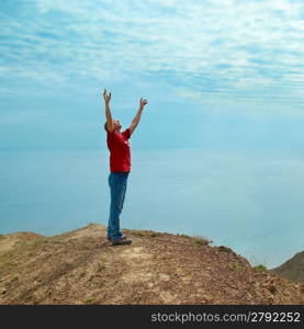 Happy man standing on the cliff with hands up looking at the sea