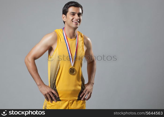 Happy man wearing gold medal with hands on hip isolated over gray background