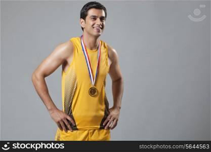 Happy man wearing gold medal with hands on hip isolated over gray background
