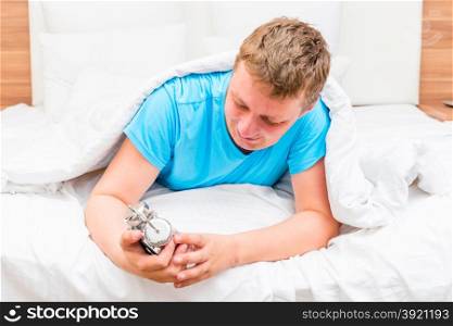 happy man with an alarm clock in hands in bed