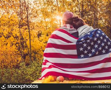 Happy married couple holding the US flag against the background of yellow trees and the setting sun. Happy relationship concept. Happy married couple holding the US flag