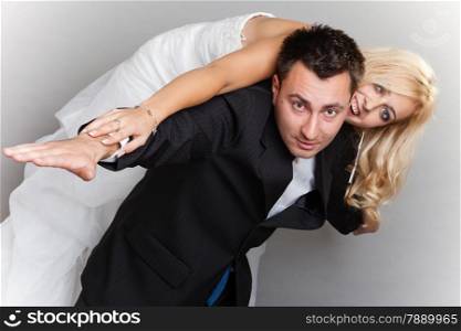 Happy married couple in love bride and groom enjoying flying, female on man&#39;s back studio shot gray background