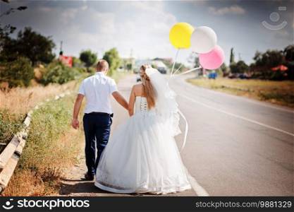 Happy married couple with balloons walk together on the road