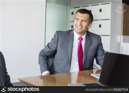 Happy mature businessman sitting at desk in office