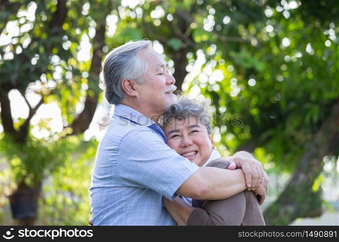 Happy mature couple in love embracing and laughing in the garden, Asian senior hugging outdoors and celebrating wedding anniversary