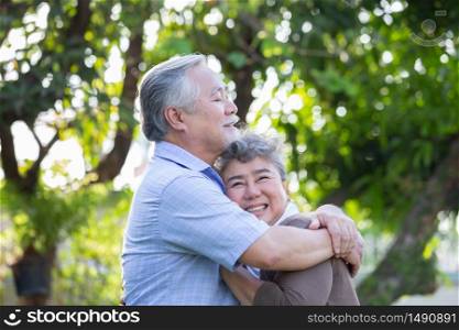 Happy mature couple in love embracing and laughing in the garden, Asian senior hugging outdoors and celebrating wedding anniversary