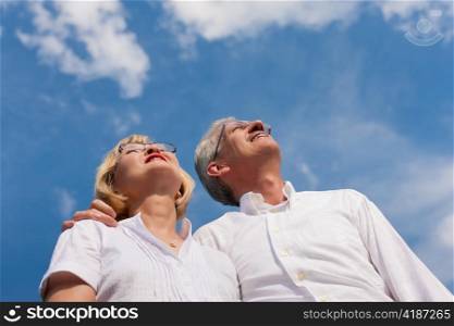 Happy mature couple - senior people (man and woman) already retired - looking to the blue sky in summer