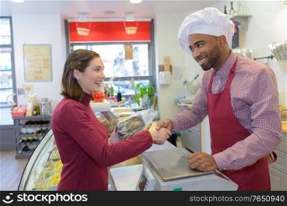 happy mature male butcher selling fresh meat to female customer