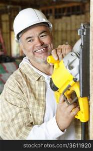Happy mature male construction worker cutting wood with a circular saw