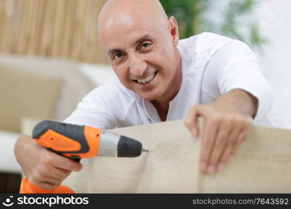 happy mature male using an electric-drill to assembly a furniture