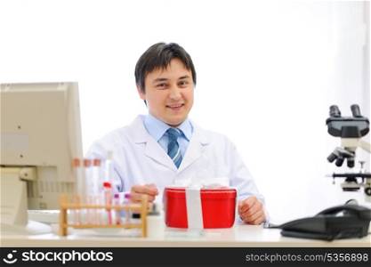 Happy medical doctor sitting at table with present box