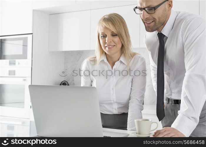 Happy mid adult business couple using laptop at kitchen counter