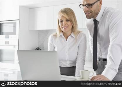 Happy mid adult business couple using laptop at kitchen counter