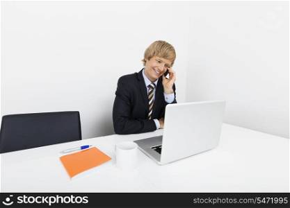 Happy mid adult businessman on call using laptop at desk in office
