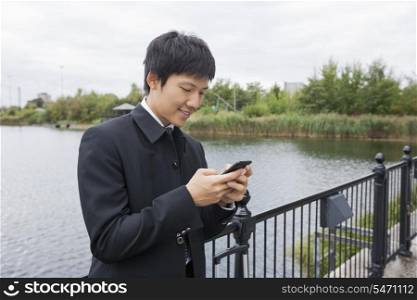 Happy mid adult businessman text messaging through mobile phone at bridge railing