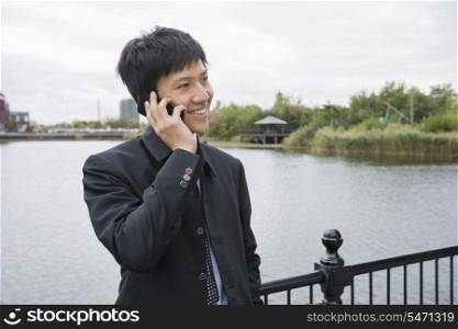 Happy mid adult businessman using cell phone at bridge railing