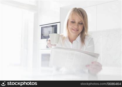Happy mid adult businesswoman having coffee while reading newspaper at home