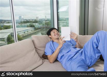 Happy mid adult man reading book while lying on sofa by window