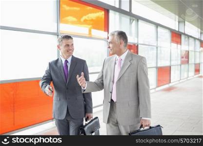 Happy middle aged businessmen talking while walking in railroad station