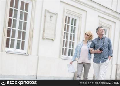Happy middle-aged tourist couple walking arm in arm by building