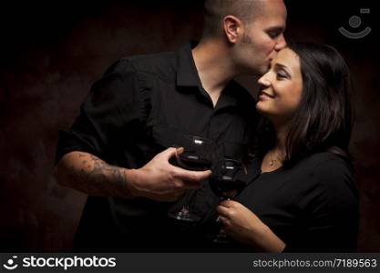 Happy Mixed Race Couple Flirting and Holding Wine Glasses on a Dark Background.