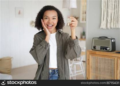 Happy mixed race girl showing keys, purchasing new house, moving to first own apartment. Overjoyed young lady tenant holding home key, rejoicing relocation. Real estate rental service advertising.. Happy mixed race girl showing keys to new home, moving to first own apartment, rejoicing relocation