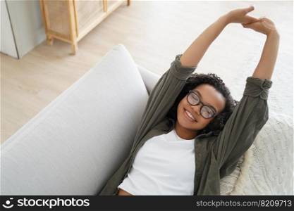 Happy mixed race girl stretching lying on sofa relaxing on weekend at home. Relaxed smiling young teen lady in glasses enjoying break pause, resting on comfortable couch. Afternoon nap, wellness.. Happy mixed race girl stretching lying on sofa relaxing on weekend at home. Afternoon nap, wellness