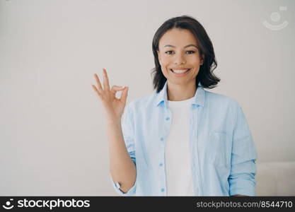 Happy mixed race lady shows ok sign. Young woman recommends. Gorgeous woman on copy space, advertiving banner mockup. Concept of approval and success. Symbol of confidence and positive emotion.. Happy mixed race lady shows ok sign. Concept of approval, success, positive emotion and confidence.